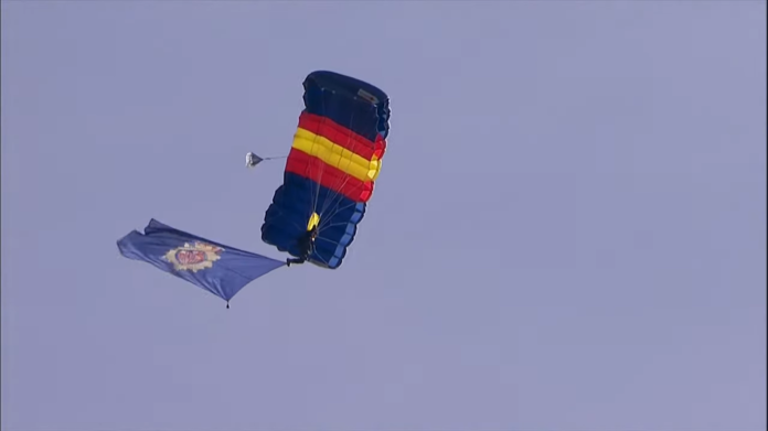 Un paracaidista porta la bandera de la policía durante el acto conmemorativo en el Palacio Real